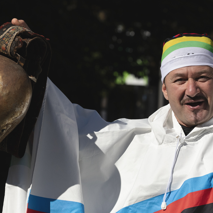 Tre Valli Varesine 2025 - A fan dressed in a UCI World Champion’s poncho holds aloft an enormous cow bell