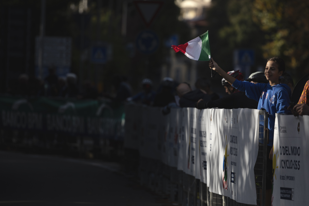 Tre Valli Varesine 2025 - A child waves an Italian flag which is caught by the sunlight
