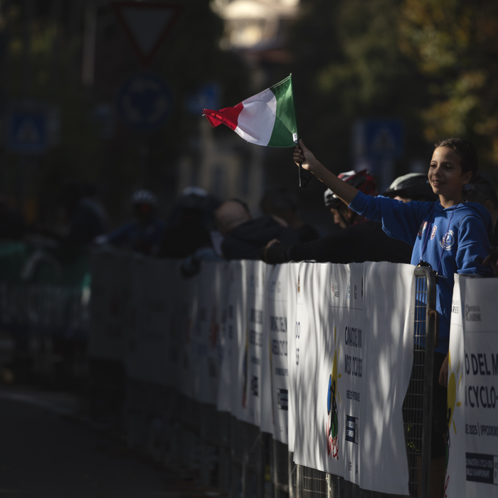 Tre Valli Varesine 2025 - A child waves an Italian flag which is caught by the sunlight