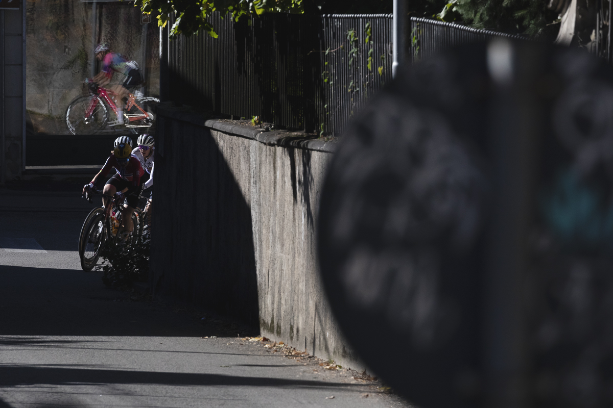 Tre Valli Varesine Women’s Race 2025 - Riders round a corner, others seen reflected in a window