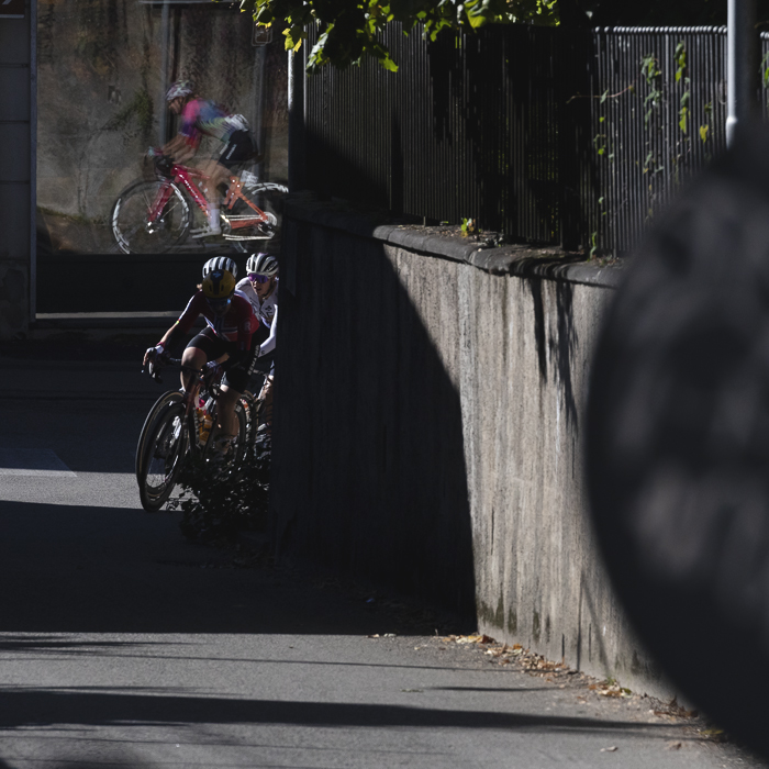 Tre Valli Varesine Women’s Race 2025 - Riders round a corner, others seen reflected in a window