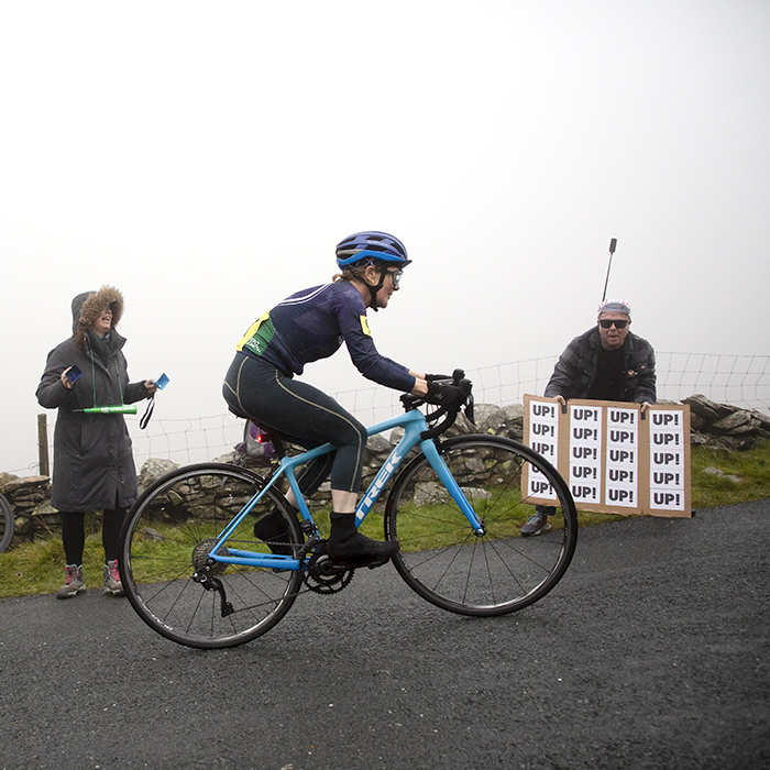 UK National Hill Climb Championships 2023 - A fan at the side of the climb holds a sign saying Up, Up, Up as Deborah John climbs
