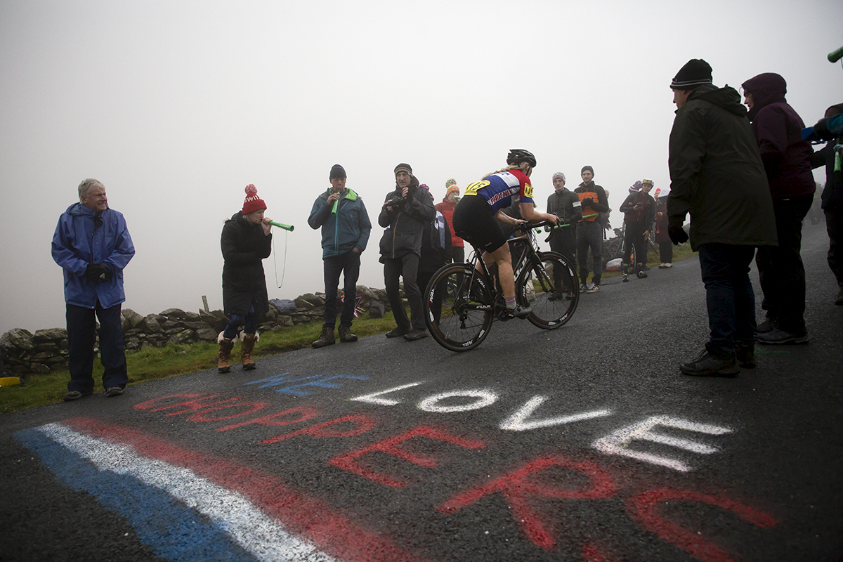 UK National Hill Climb Championships 2023 - Louise Johnson rides over red, white and blue writing on the road that reads We Love Choppers as fans blow vuvuzelas