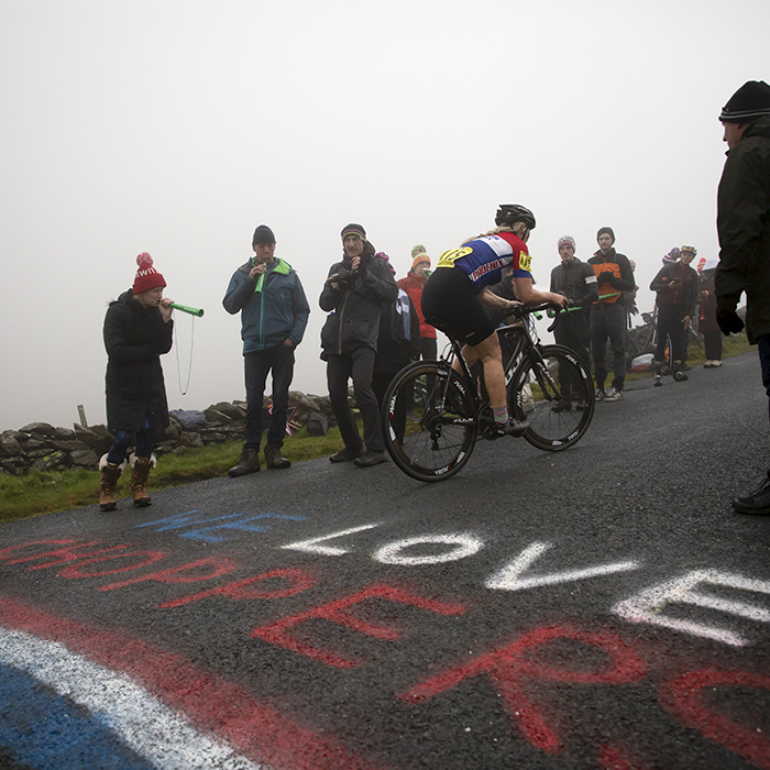 UK National Hill Climb Championships 2023 - Louise Johnson rides over red, white and blue writing on the road that reads We Love Choppers as fans blow vuvuzelas