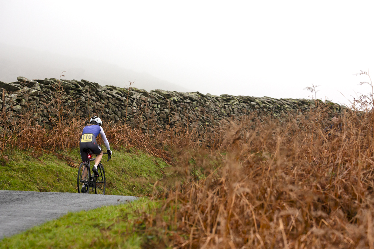 UK National Hill Climb Championships 2023 - Sally Cunliffe from behind as she passes dry stone walls and verges with brown bracken