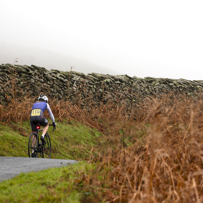 UK National Hill Climb Championships 2023 - Sally Cunliffe from behind as she passes dry stone walls and verges with brown bracken